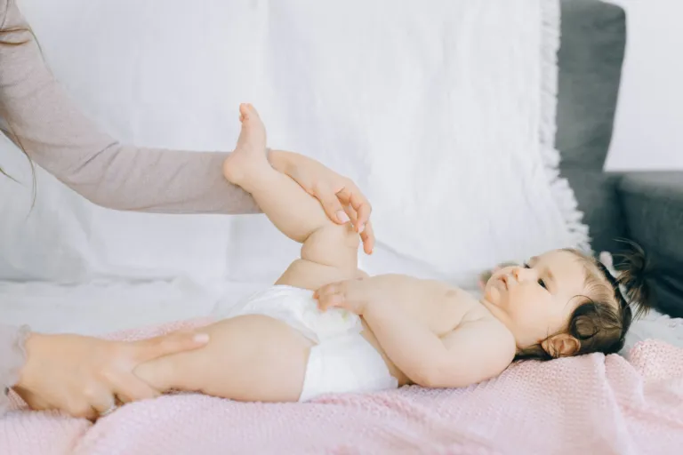 Bébé allongé sur le dos dont les mains d'un adulte mobilisent doucement la jambe