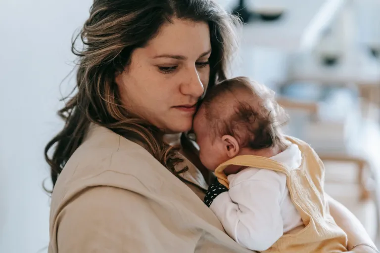Mère serrant tendrement son nourrisson contre sa joue, dans une lumière douce