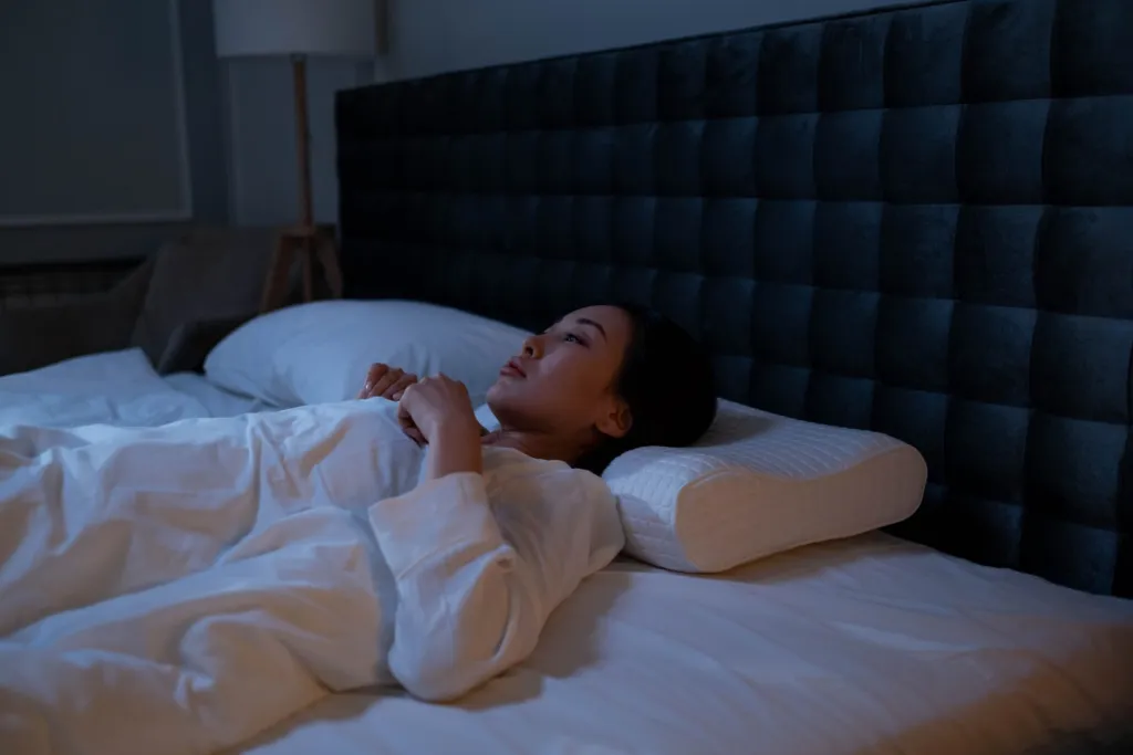 Femme allongée dans son lit la nuit, éveillée, le regard tourné vers le plafond