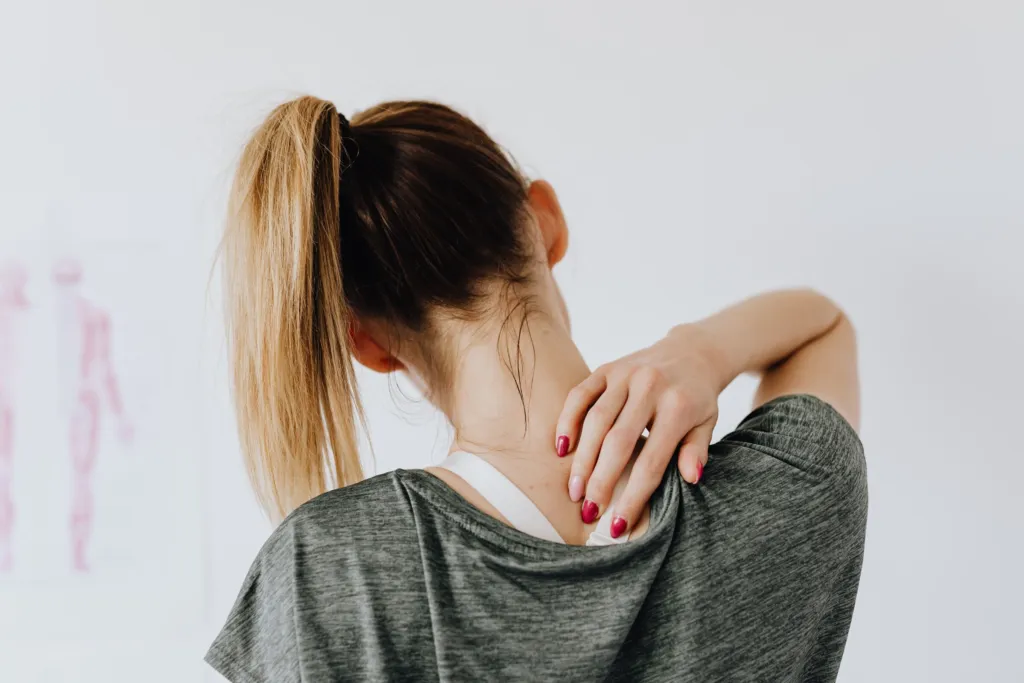 Femme vue de dos, une main posée sur le haut de son dos douloureux