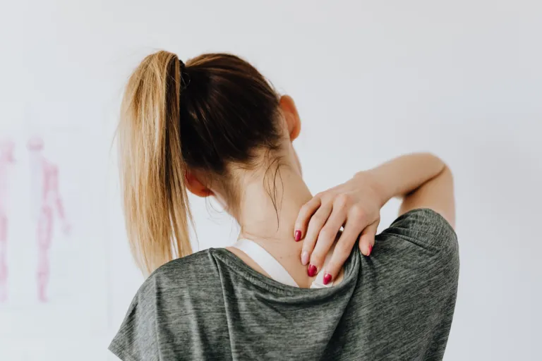Femme vue de dos, une main posée sur le haut de son dos douloureux