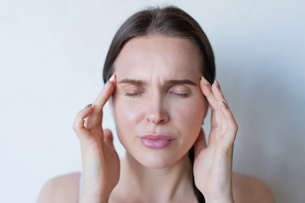 Femme aux yeux fermés, les doigts posés sur les tempes, sur fond clair