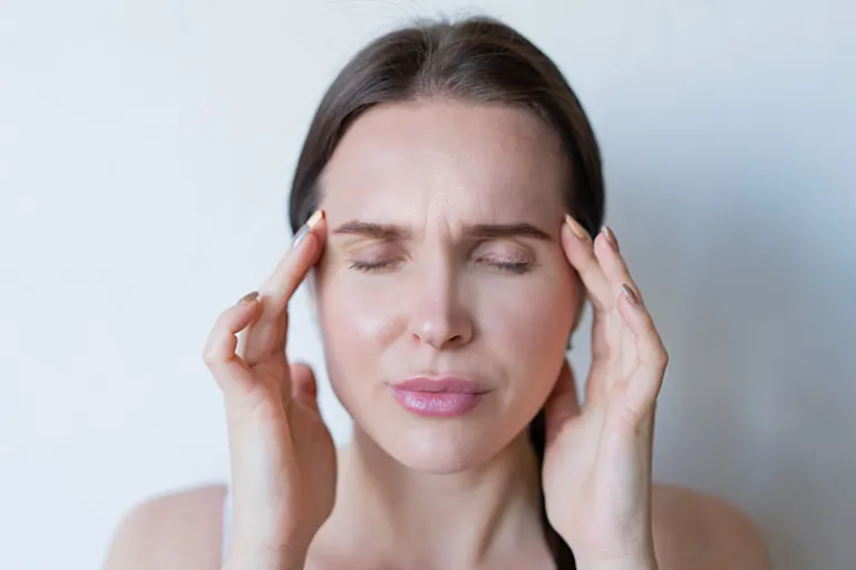 Femme aux yeux fermés, les doigts posés sur les tempes, sur fond clair