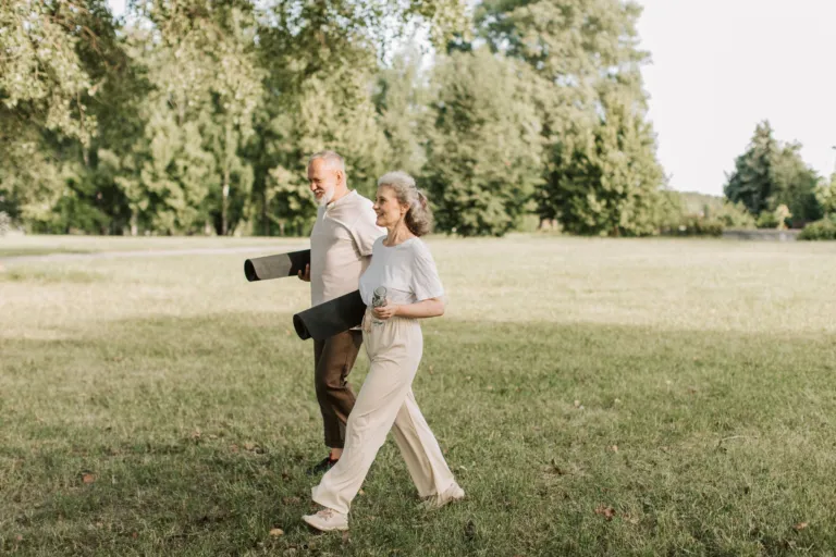 Couple de seniors souriants marchant dans un parc, tapis de yoga sous le bras