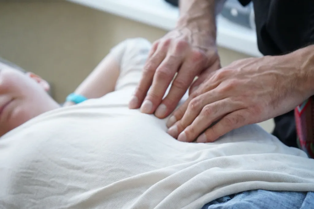 Deux mains posées en douceur sur le ventre d'une personne allongée et habillée