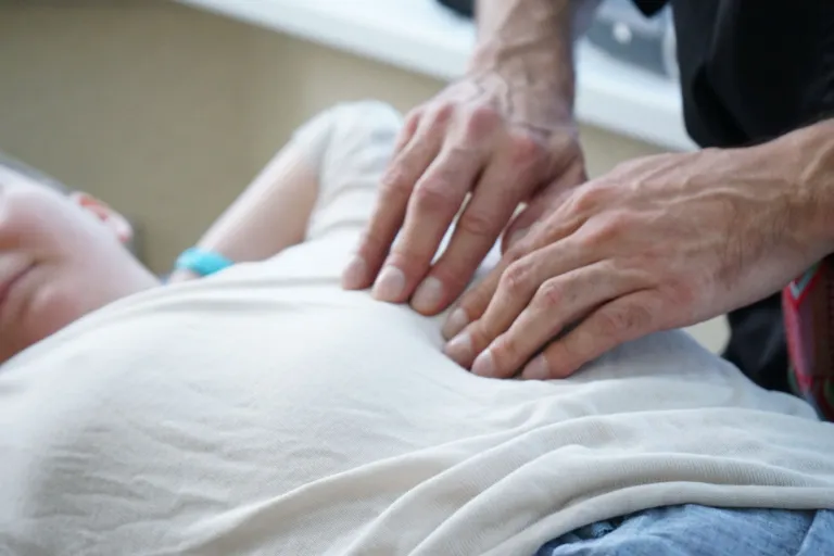 Deux mains posées en douceur sur le ventre d'une personne allongée et habillée