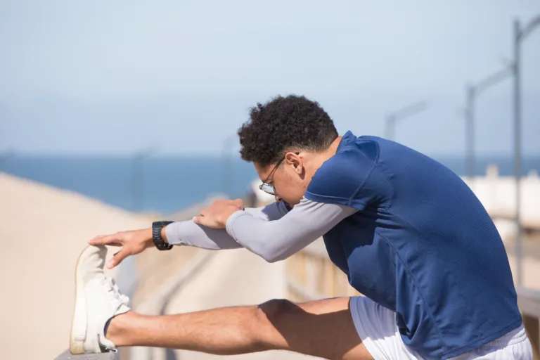 Homme en tenue de sport étirant sa jambe, avec la mer en arrière-plan
